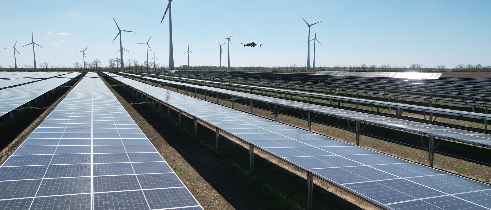 Freiflächen-PV-Anlage mit Windrädern, Drohne im Anflug